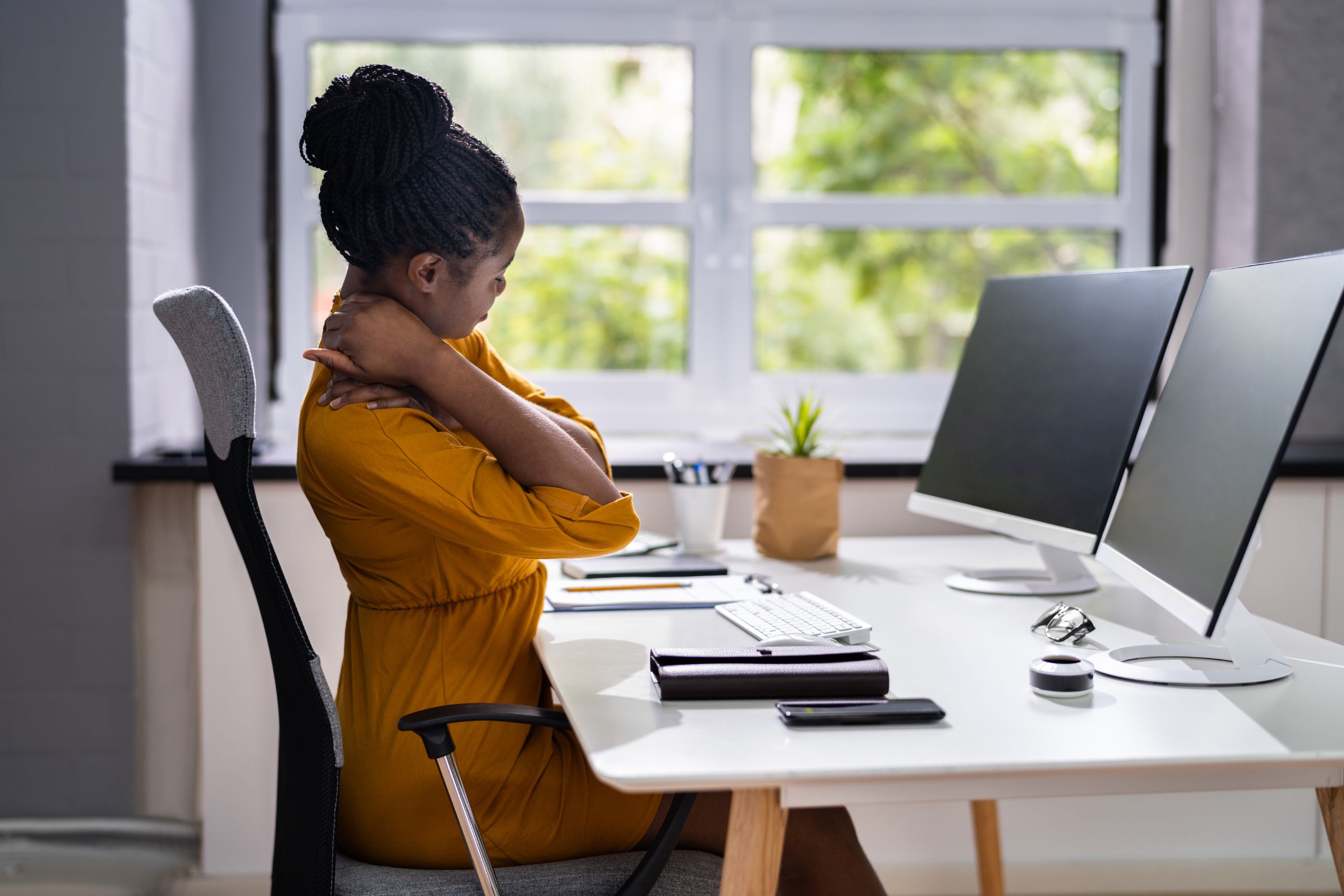 woman sitting at office desk rubbing her neck in pain because she needs better workplace ergonomics